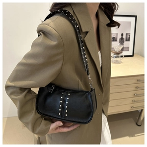 Détail d'un sac baguette en similicuir noir à rivets argentés porté par un mannequin chic