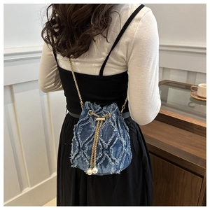 Détail du sac seau en denim bleu avec motif à franges et bandoulière en perles
