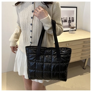 Detail of a large black quilted tote bag with wide straps shown in a lifestyle setting
