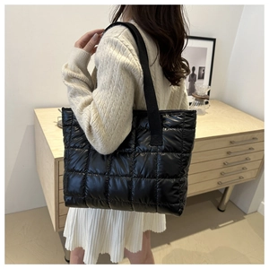 Modern black quilted tote bag with wide straps shown in a minimalist interior setting