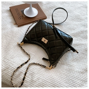Close-up of black quilted leather shoulder bag with gold chain and twist lock on fabric