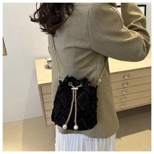 Détail du sac seau noir avec texture matelassée, chaîne dorée et perle élégante