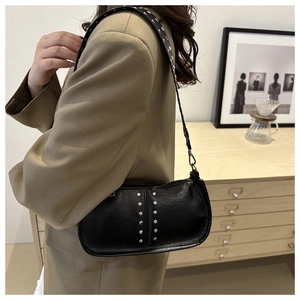Détail d'un sac bandoulière noir avec rivets argentés porté dans un décor d'intérieur