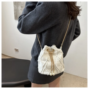 Dettaglio borsa a secchiello bianca con bordi sfrangiati, catena dorata e ciondoli di perle