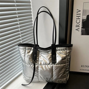 Modern silver quilted tote bag with black leather straps shown in a minimalist setting