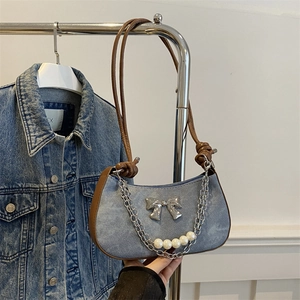 Blue denim underarm bag with metal bow and pearl chain hanging on a metal hanger
