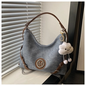 Detail of grey canvas tote bag with brown straps, metal M logo and plush cloud charm