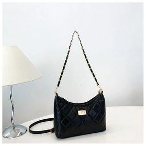 Close-up of black quilted leather texture and gold metal twist lock on a tote bag