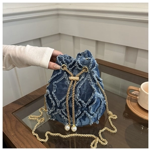 Détail du sac seau en jean bleu avec franges et bandoulière perle sur une table