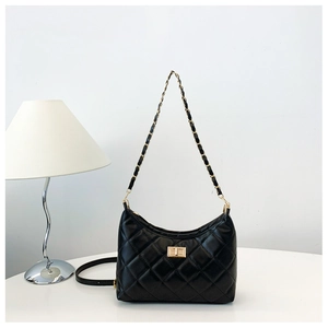 Detail of black quilted chain tote bag with golden lock on minimalist white desk