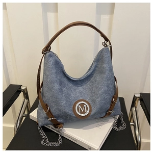 Close-up of blue denim tote bag with brown leather straps and silver metal M logo