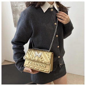 Detail of gold quilted crossbody bag with silver butterfly clasp and chain strap