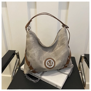 Detail of taupe canvas tote with leather straps and silver M logo on a black chair