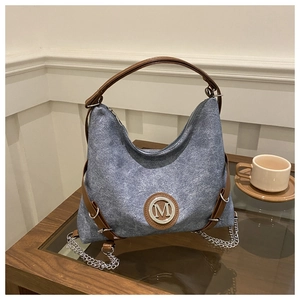 Close-up of blue denim tote bag with brown leather handles and metallic M logo