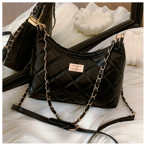 Macro detail of black quilted leather texture and gold metal chain strap on tote bag