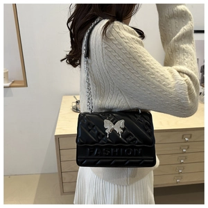 Detail of black quilted shoulder bag featuring silver butterfly clasp and fashion lettering