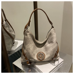 Detail of grey canvas tote bag with brown leather strap and circular metal M logo