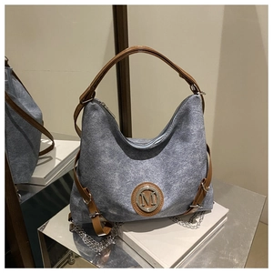 Macro detail of denim blue tote with brown leather handles and metallic M logo