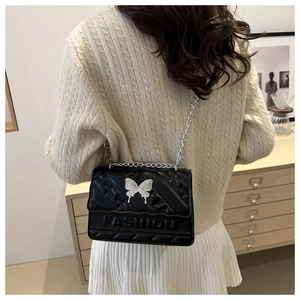 Detailed close-up of quilted black leather crossbody bag with silver butterfly ornament