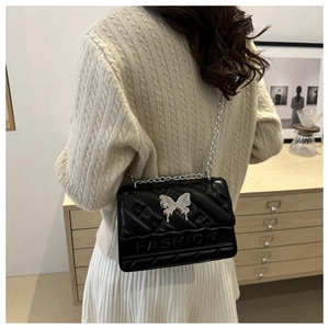 Detail of black crossbody bag with silver butterfly charm and metal chain strap