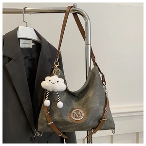 Détail d'un sac cabas en toile grise avec lanières en cuir brun et breloque nuage