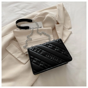 Detail of black quilted crossbody bag with FASHION embossing on a beige blazer