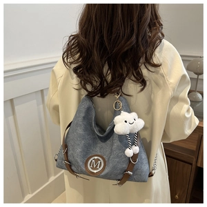 Detail of grey-blue Hobo bag featuring a metal M logo and plush cloud charm accessory