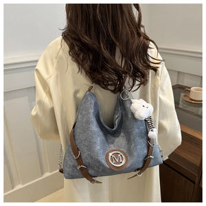 Detail of grey denim tote bag with leather straps and plush cloud charm on model