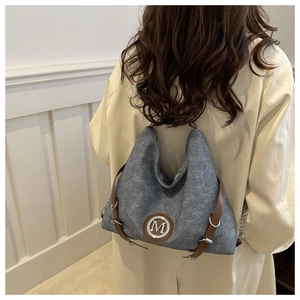 Détail macro du sac hobo gris texturé avec lanière en cuir brun et boucle M en argent