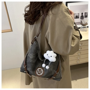 Detail of grey canvas hobo bag featuring brown leather trim and a white cloud plush charm