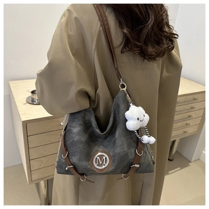 Détail du sac hobo en toile grise avec logo M, lanières en cuir et charme nuage