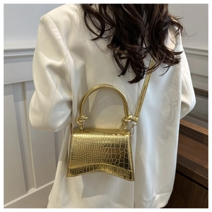Detailed view of golden crocodile textured hourglass handbag with knotted handles and strap