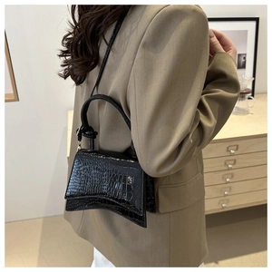 Detail view of the black crocodile pattern texture and curved base of the small square bag