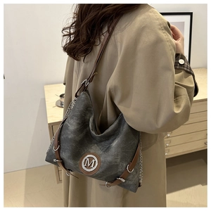 Detail of grey canvas tote with leather M logo and adjustable shoulder strap worn by model