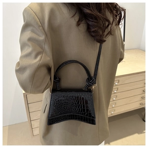 Detail of black glossy crocodile pattern crossbody bag showing the unique curved bottom design