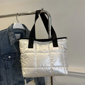 Quilted white space cotton tote bag with black straps hanging in a minimalist setting