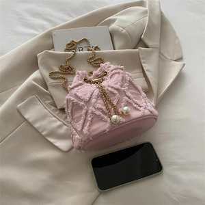 Sac seau en denim rose avec cordon de perles et chaîne dorée sur blazer beige