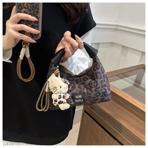 Détail d'un sac à main léopard avec poignée noire et pendentif chat blanc en peluche