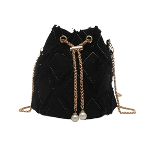 Sac seau noir matelassé avec bords effilochés et détails de perles sur fond blanc