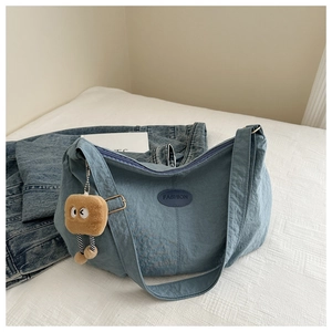 Close-up of blue nylon tote with a leather logo patch and bread-shaped plush charm