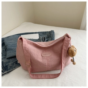Detail of light pink fabric crossbody bag with FASHION patch and plush biscuit charm