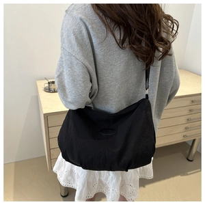 Detail of minimalist black nylon tote bag with logo patch and wide shoulder strap