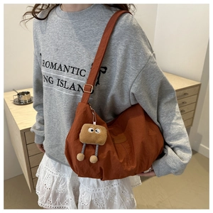 Burnt orange nylon tote bag with plush keychain shown on model in a cozy setting