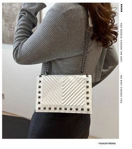Detail of white quilted handbag with grey square studs and heavy dark metal chain strap
