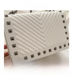Close-up of white quilted shoulder bag featuring square metal studs and chain strap