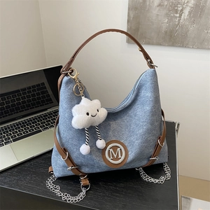 Chic blue denim tote bag with brown leather straps and metal M logo on office desk