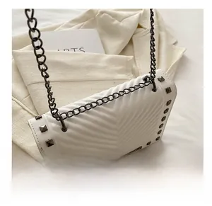 Detail of white V-quilted shoulder bag with grey studs on a suit background