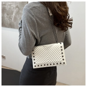 Close-up of white V-quilted crossbody bag with black stud rivets and chain strap on model