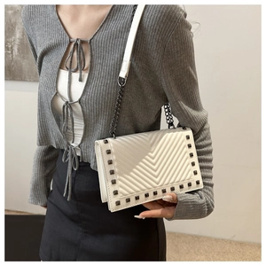 Detail of white V-quilted crossbody bag with stud rivets and chain strap on model