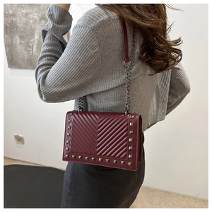 Detail of burgundy V-quilted shoulder bag with silver square studs and chain strap